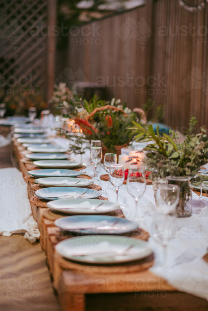 Outdoor dining setup with elegant tableware and seasonal flowers at sunset - Australian Stock Image