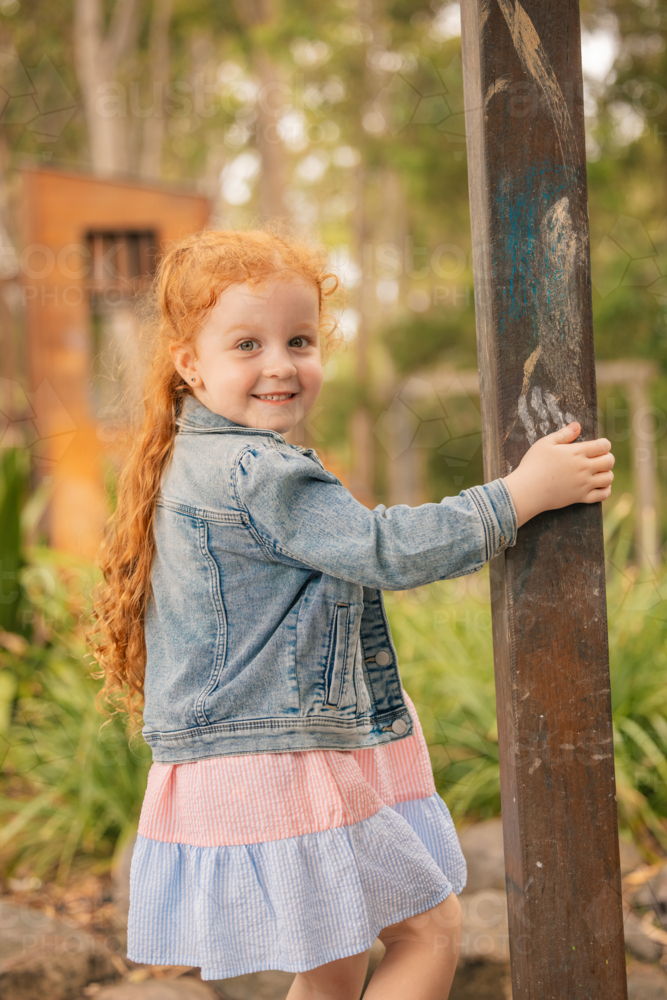 Outdoor portrait of happy preschool age girl with long red hair at kindergarten - Australian Stock Image