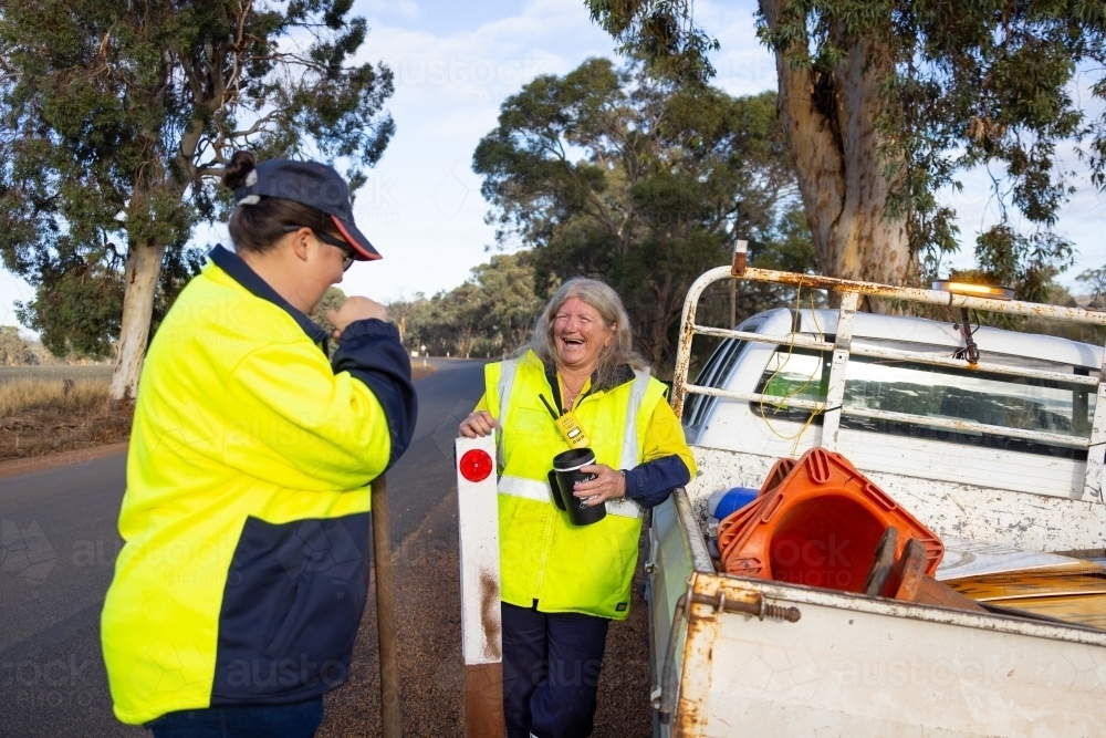 outdoor workers wearing hi-vis workwear having a break at side of road - Australian Stock Image