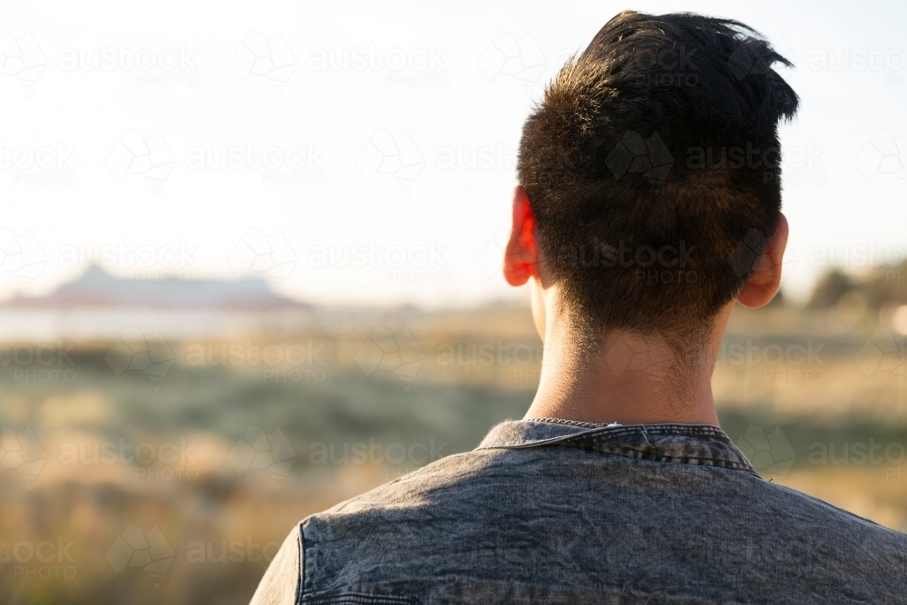 Over shoulder shot of young latino male looking out over coastal scrub - Australian Stock Image