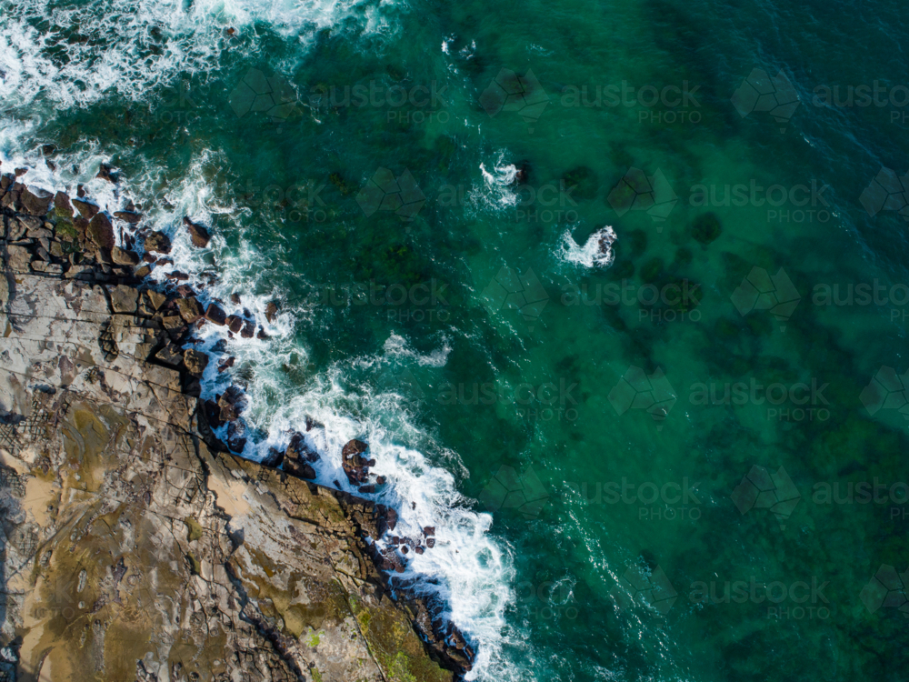 Overhead coastal view of rocky Australian coastline with waves foaming white around boulders in sea - Australian Stock Image