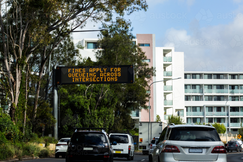 Overhead digital sign displaying fines apply for queueing across intersection above road in Sydney - Australian Stock Image