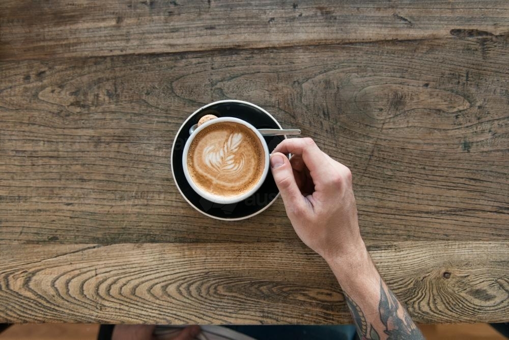 Overhead image of a coffee on a wooden table with customer's arm - Australian Stock Image