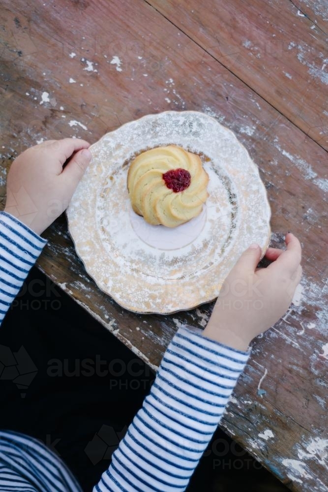 overhead of child with biscuit on a vintage plate - Australian Stock Image