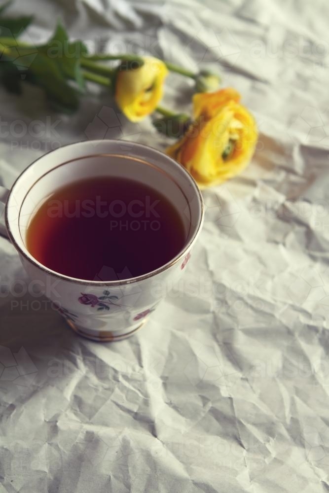 Overhead of cup of tea in vintage cup with yellow roses on crumpled paper background - Australian Stock Image