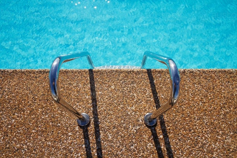 Overhead of pebble mix swimming pool edge with ladder forming graphic elements - Australian Stock Image