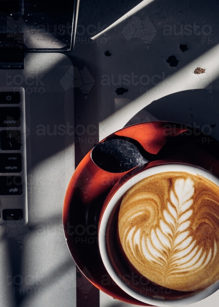 Overhead shot of a mug of coffee beside the corner of a laptop - Australian Stock Image