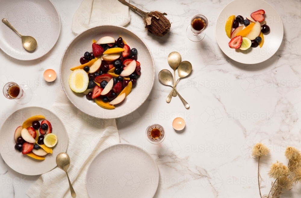 Overhead shot of dinner party mixed fruit salad dessert on marble table with candles - Australian Stock Image