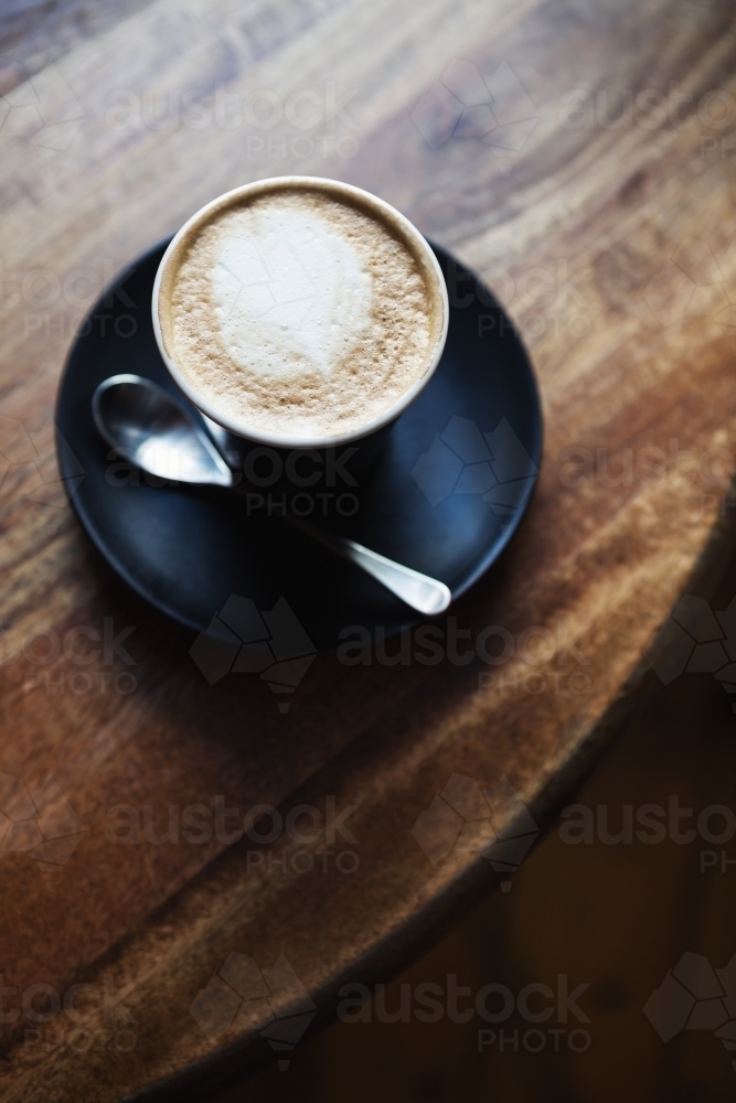 Overhead view of cafe latte in black ceramic cup on a wooden restaurant table - Australian Stock Image
