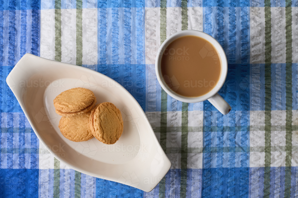 overhead view of Monte Carlo biscuits with coffee cup on blue tablecloth - Australian Stock Image