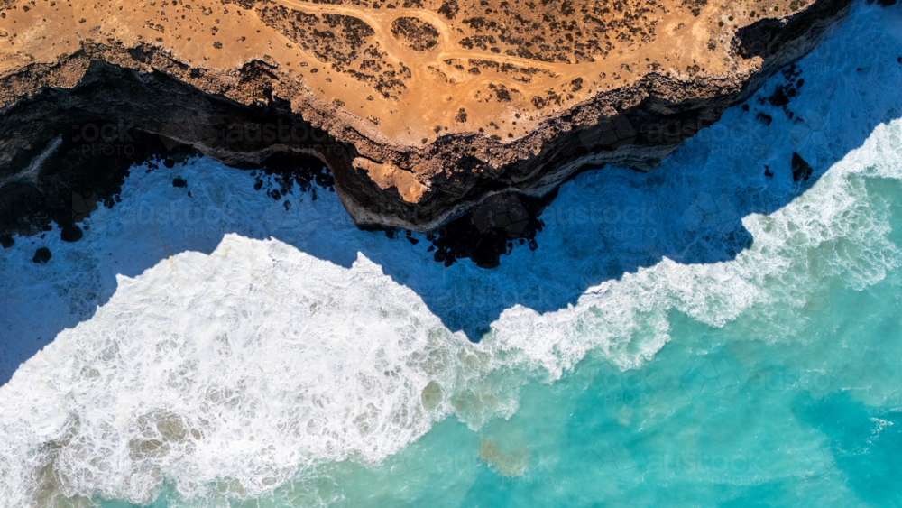 Overhead view of towering cliffs with strong waves crashing through creating foam - Australian Stock Image