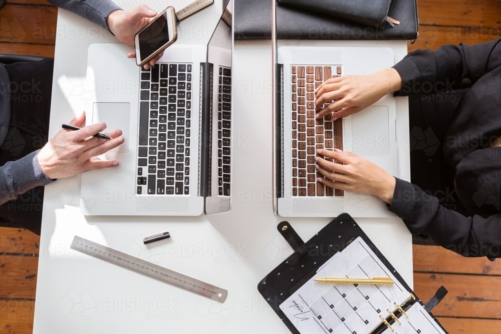 Overhead view of two people working on their laptop keyboards - Australian Stock Image
