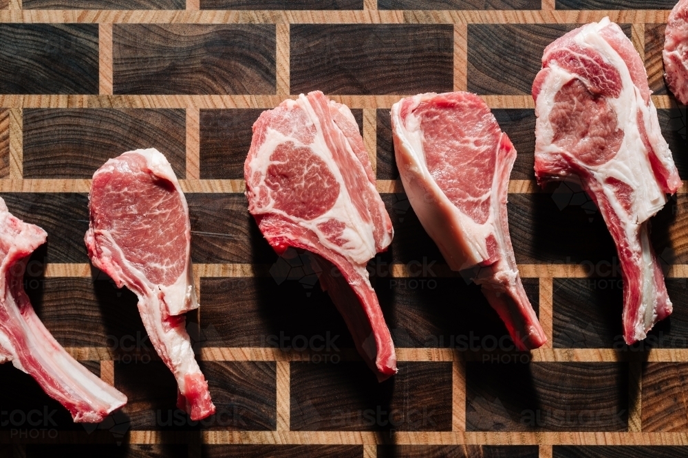 Overhead view of uncooked lamb cutlets arranged on a wooden chopping board - Australian Stock Image