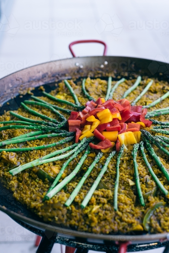 paella topped with asparagus and capsicum on an outdoor pan - Australian Stock Image