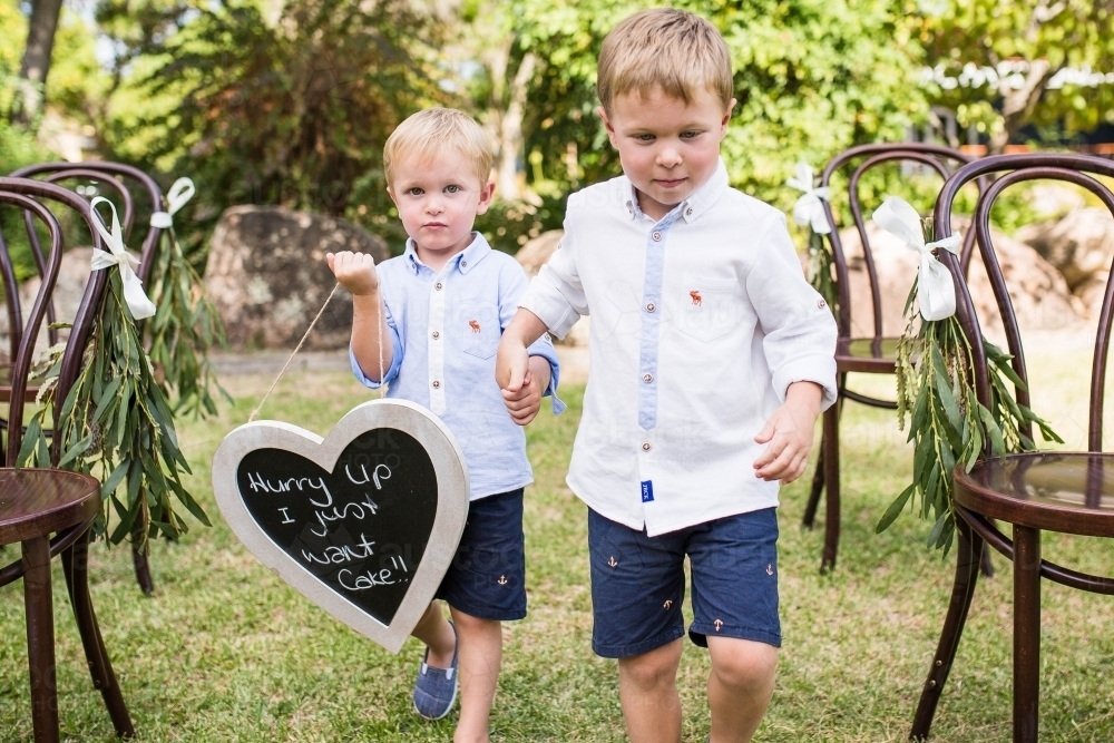 Pageboys walking down aisle holding hands holding sign - Australian Stock Image