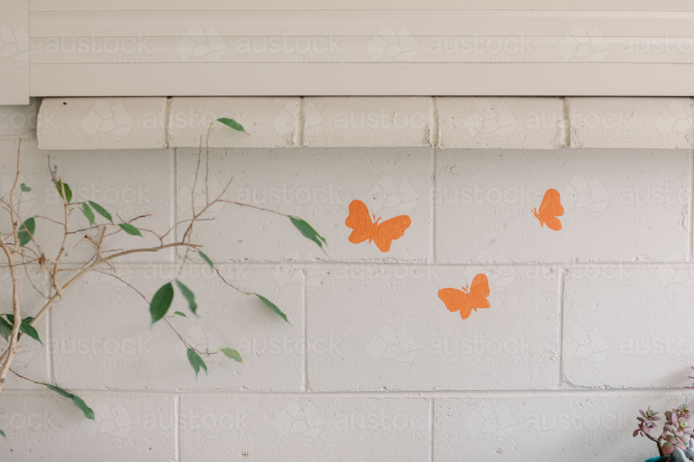 painted brick wall with butterfly stickers and twigs with leaves - Australian Stock Image