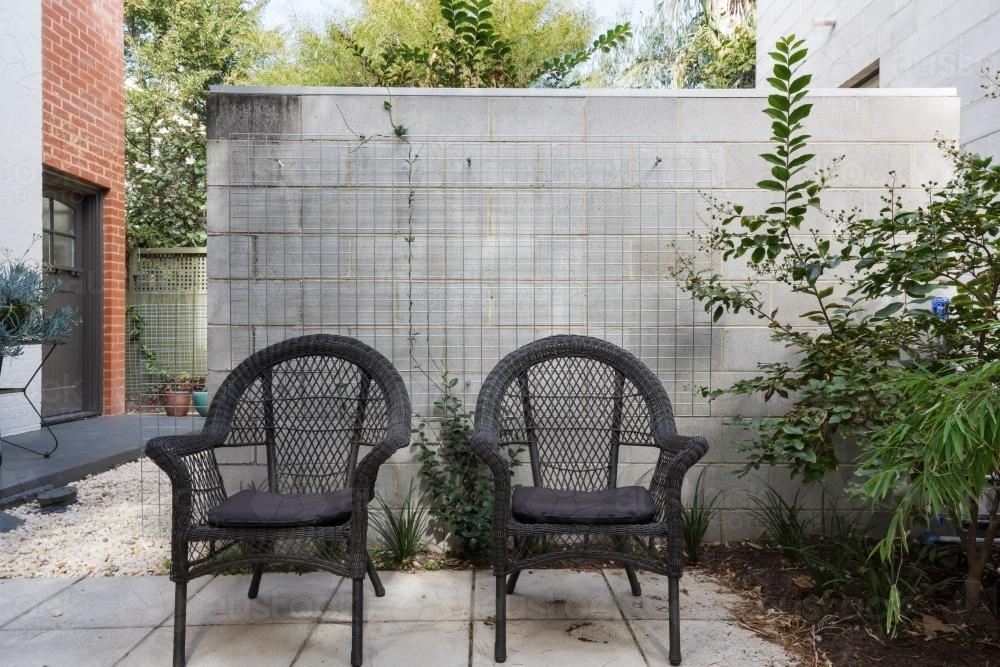 Pair of black cane outdoor chairs in modern paved apartment courtyard - Australian Stock Image