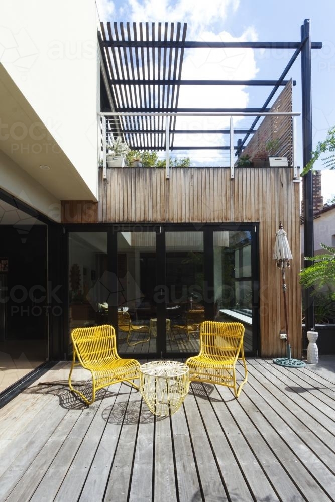 Pair of yellow cane outdoor chairs on wooden deck in contemporary courtyard - Australian Stock Image