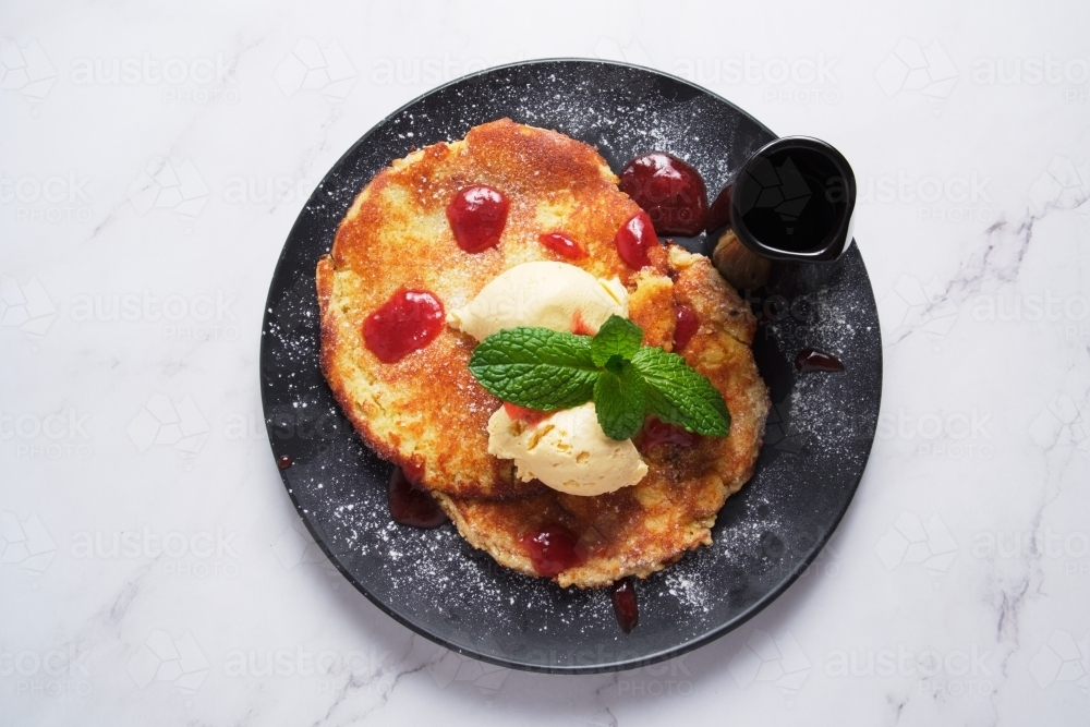 Pancakes served in a black plate topped with butter and mint - Australian Stock Image