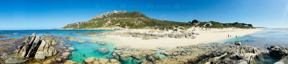 Panorama of remote idyllic beach with clear water, rocks and small figures on beach - Australian Stock Image