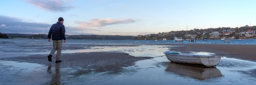 Panoramic photo of early morning walker on sand flats near a small boat - Australian Stock Image