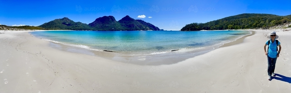 Panoramic photo of the beach at Wineglass Bay with a person walking - Australian Stock Image