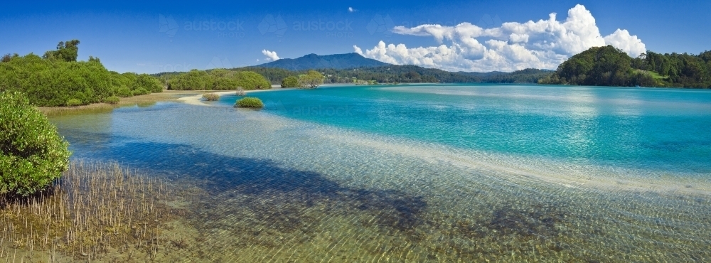 Panoramic view of a blue freshwater estuary with mangroves on its edge and cloud in the background - Australian Stock Image