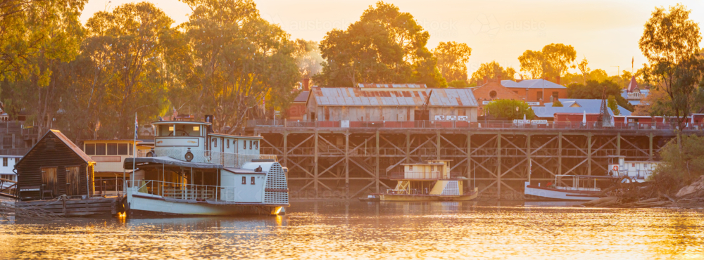 Panorma view of historic paddle steamers beside an old river port in golden evening light - Australian Stock Image