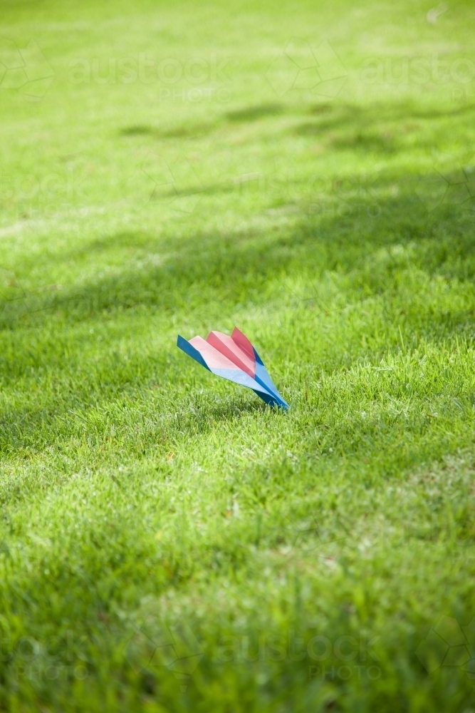 Paper plane nose dive onto green hill - Australian Stock Image