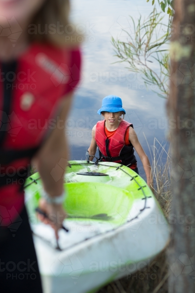 Parent and child hauling a kayak out of river - Australian Stock Image