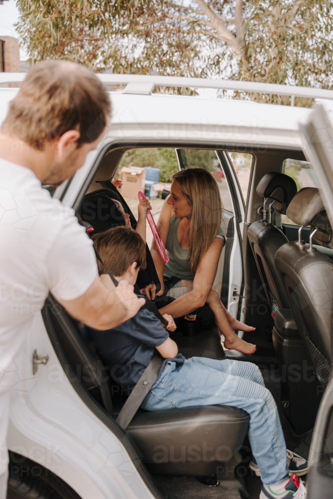 Parents helping the kids secure them in the car and booster seat. - Australian Stock Image