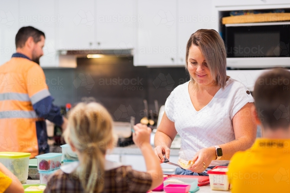 Parents in kitchen making lunches for school kids as the family eats breakfast - Australian Stock Image