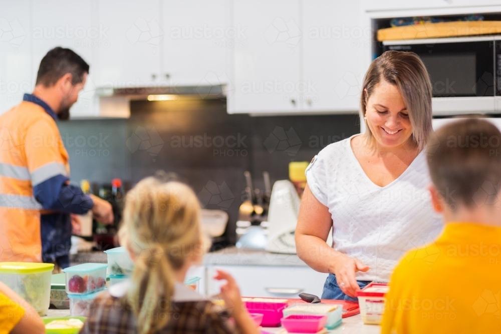 Parents in kitchen making lunches for school kids as the family eats breakfast - Australian Stock Image