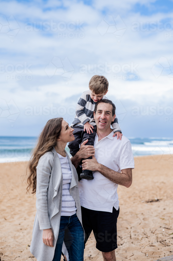 Parents joyfully interacting with their son during a beach day on a cloudy afternoon - Australian Stock Image