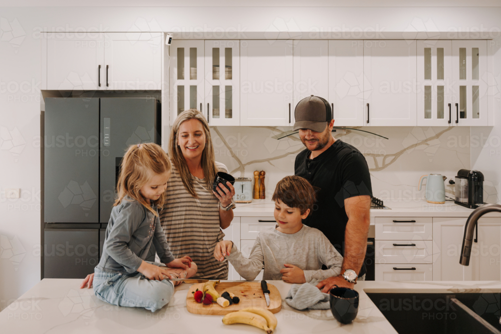 Parents teaching kids how to cut fruits in the kitchen. - Australian Stock Image