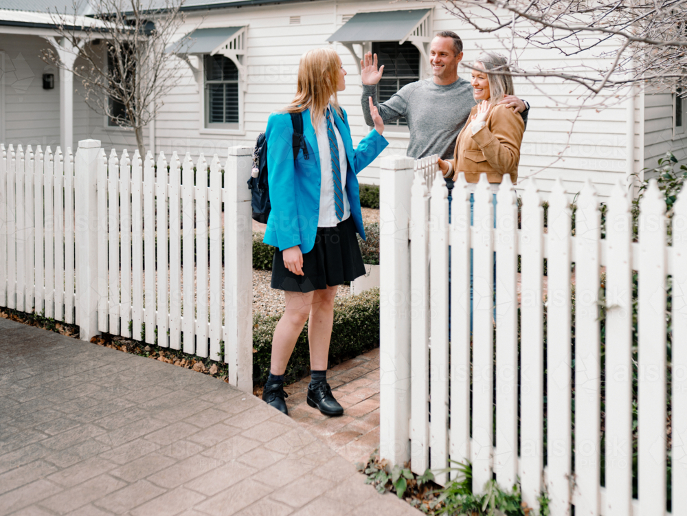 Parents waving goodbye to teenage daughter leaving for school on sunny day - Australian Stock Image