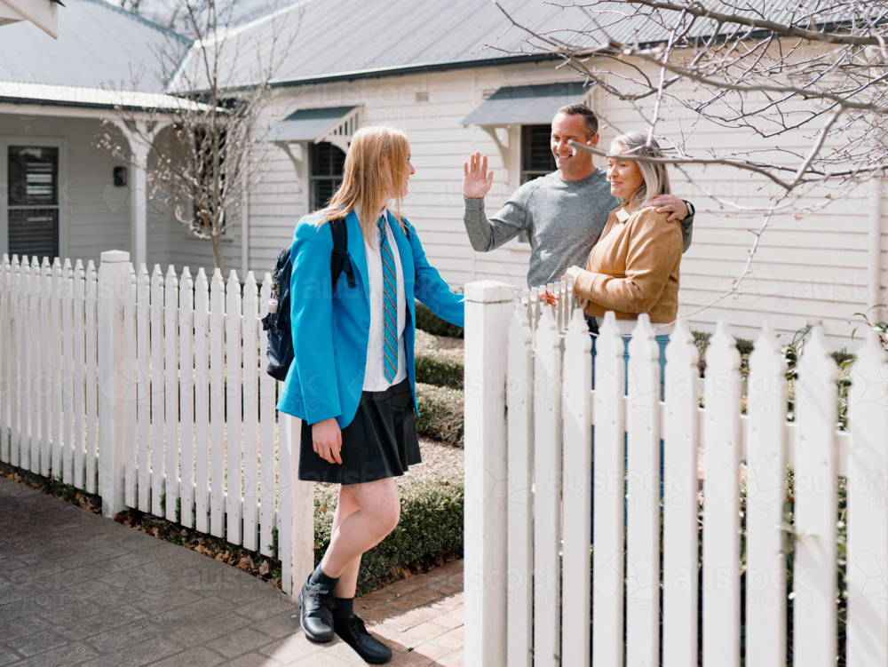 Parents waving goodbye to teenage daughter leaving for school on sunny day - Australian Stock Image