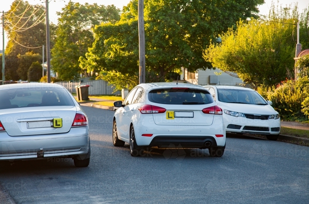 Parked car with l plate and another learner driver passing on quiet road - Australian Stock Image