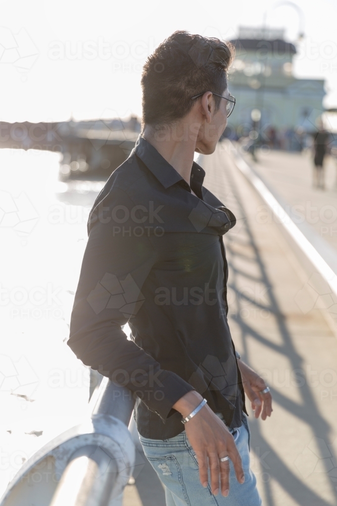 Partially backlit portrait of hispanic male leaning on pier railing - Australian Stock Image