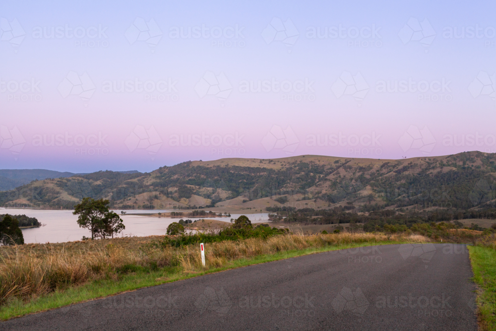 Pastel dusk sky over road through landscape of farm paddocks beside Lake St Clair NSW - Australian Stock Image