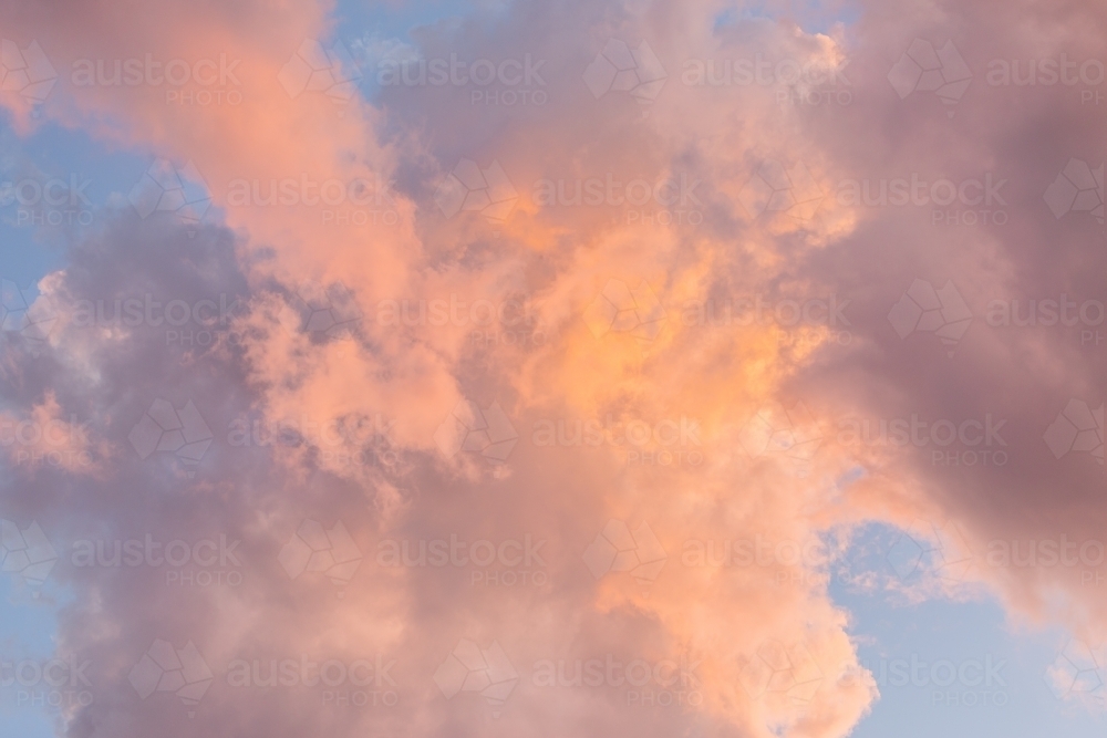 Pastel pink cloud in light blue sky at dusk - Australian Stock Image