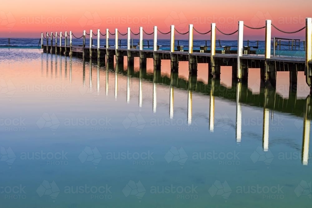 Pastel sunrise reflected off water at ocean baths Narrabeen - Australian Stock Image