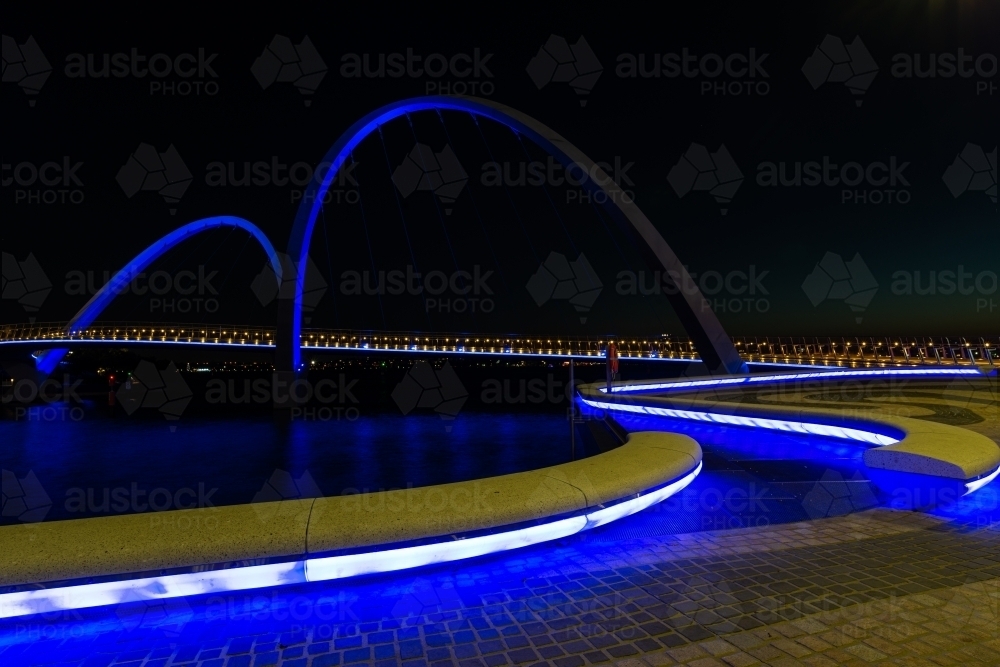 Path curving onto arched bridge with blue lighting and night sky - Australian Stock Image