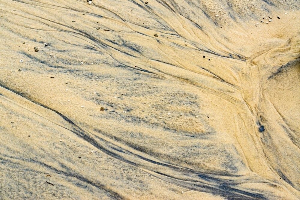 Patterns in wet yellow and black mineral sands on a beach at low tide - Australian Stock Image