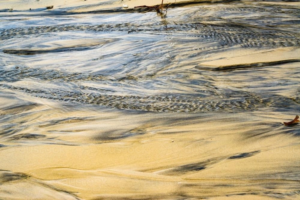 Patterns in wet yellow and black mineral sands on a beach at low tide - Australian Stock Image