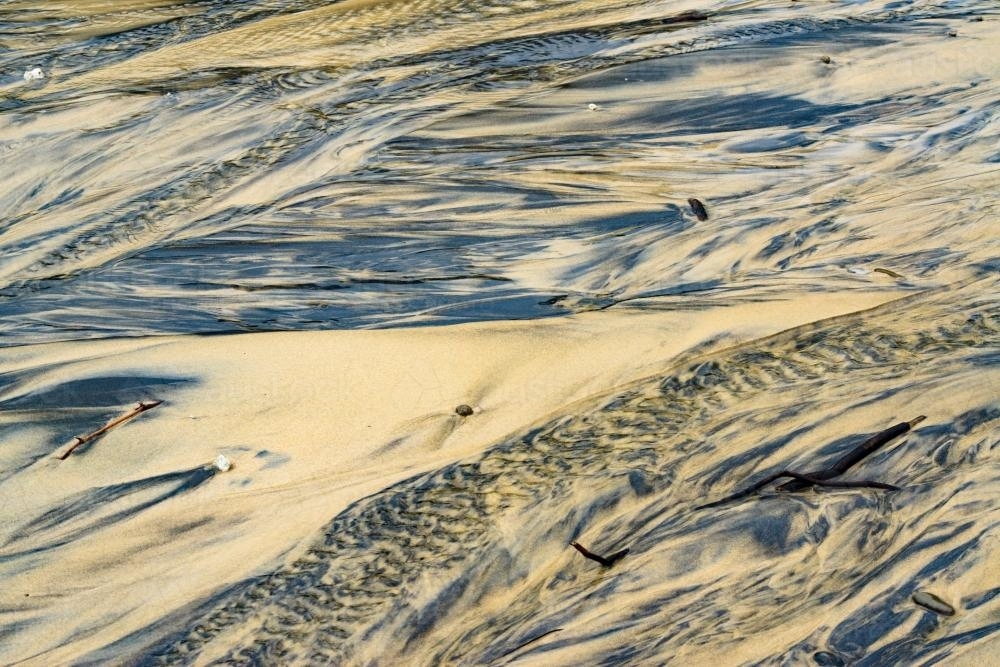 Patterns in wet yellow and black mineral sands on a beach at low tide - Australian Stock Image