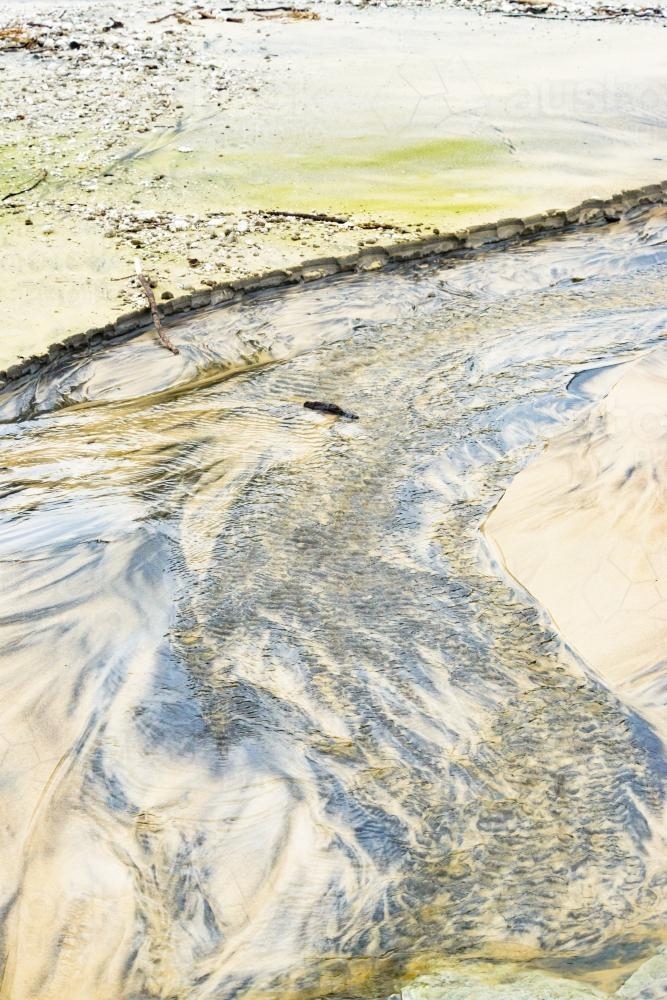 Patterns in wet yellow and black mineral sands on a beach at low tide - Australian Stock Image