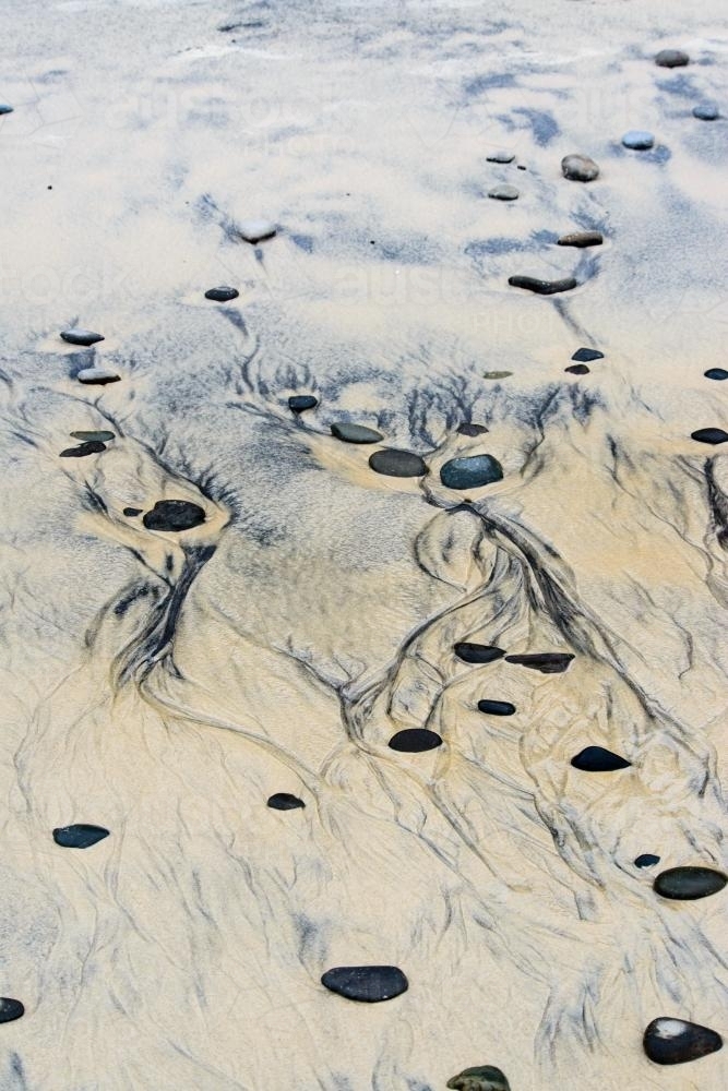 Patterns in wet yellow and black mineral sands on a beach at low tide with pebbles - Australian Stock Image