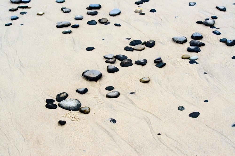 Patterns in wet yellow and black mineral sands on a beach at low tide with pebbles - Australian Stock Image