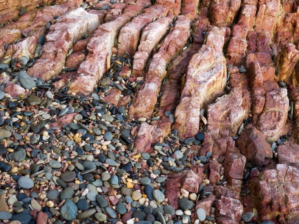 Patterns of red rock and smooth pebbles on a beach - Australian Stock Image